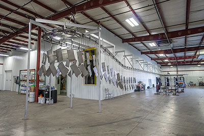 Parts hang from a conveyor belt prior to pressure wash for powder coating.